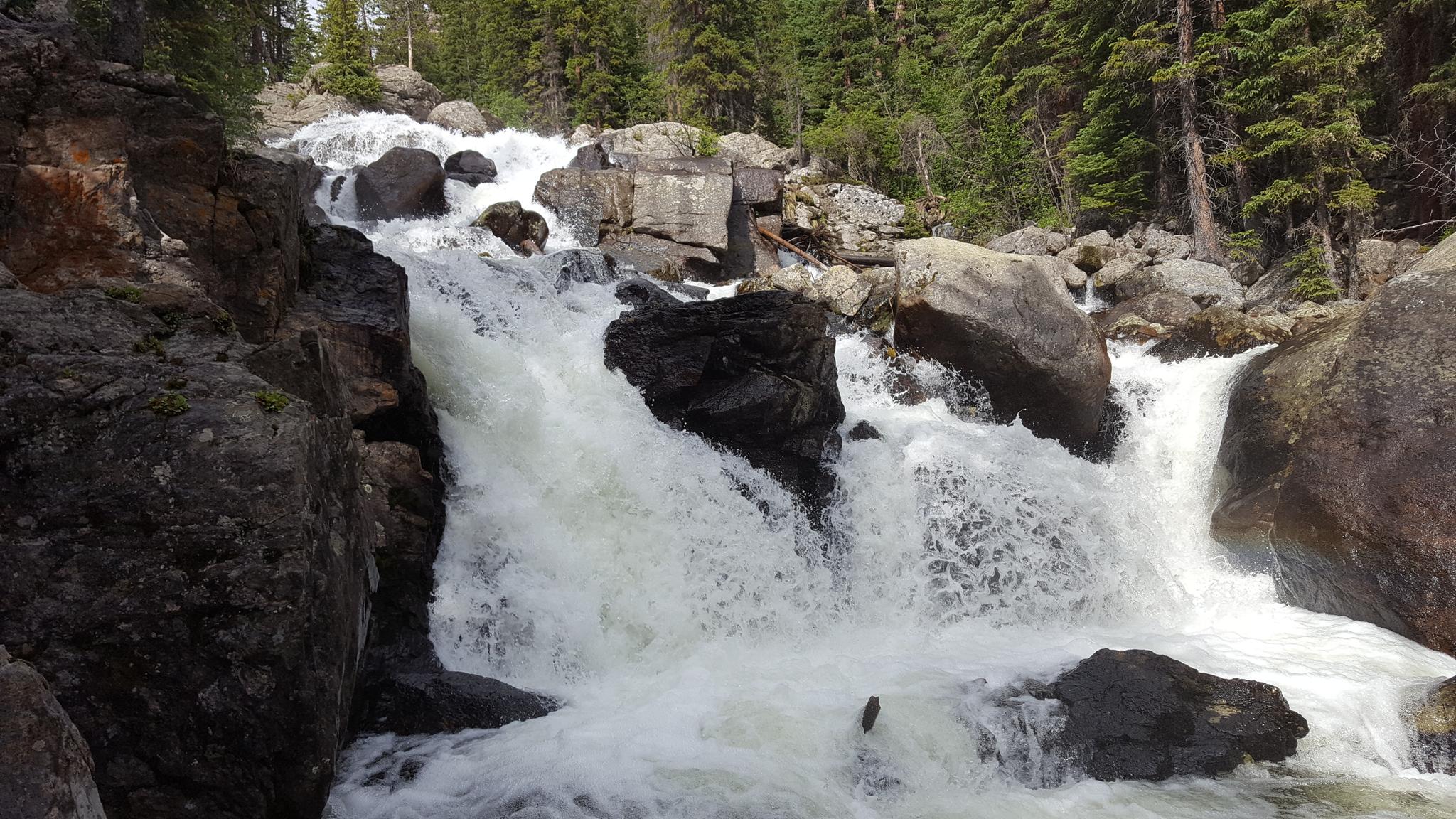 Powerful waterfall cascading over large rocks amidst green forest in bright daylight.