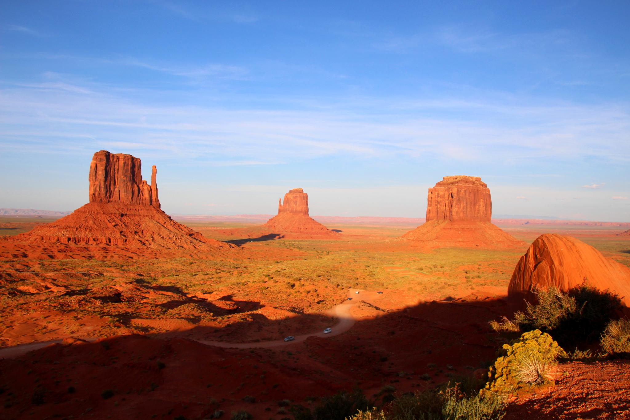Three prominent red rock formations in a desert landscape at sunset, casting long shadows.