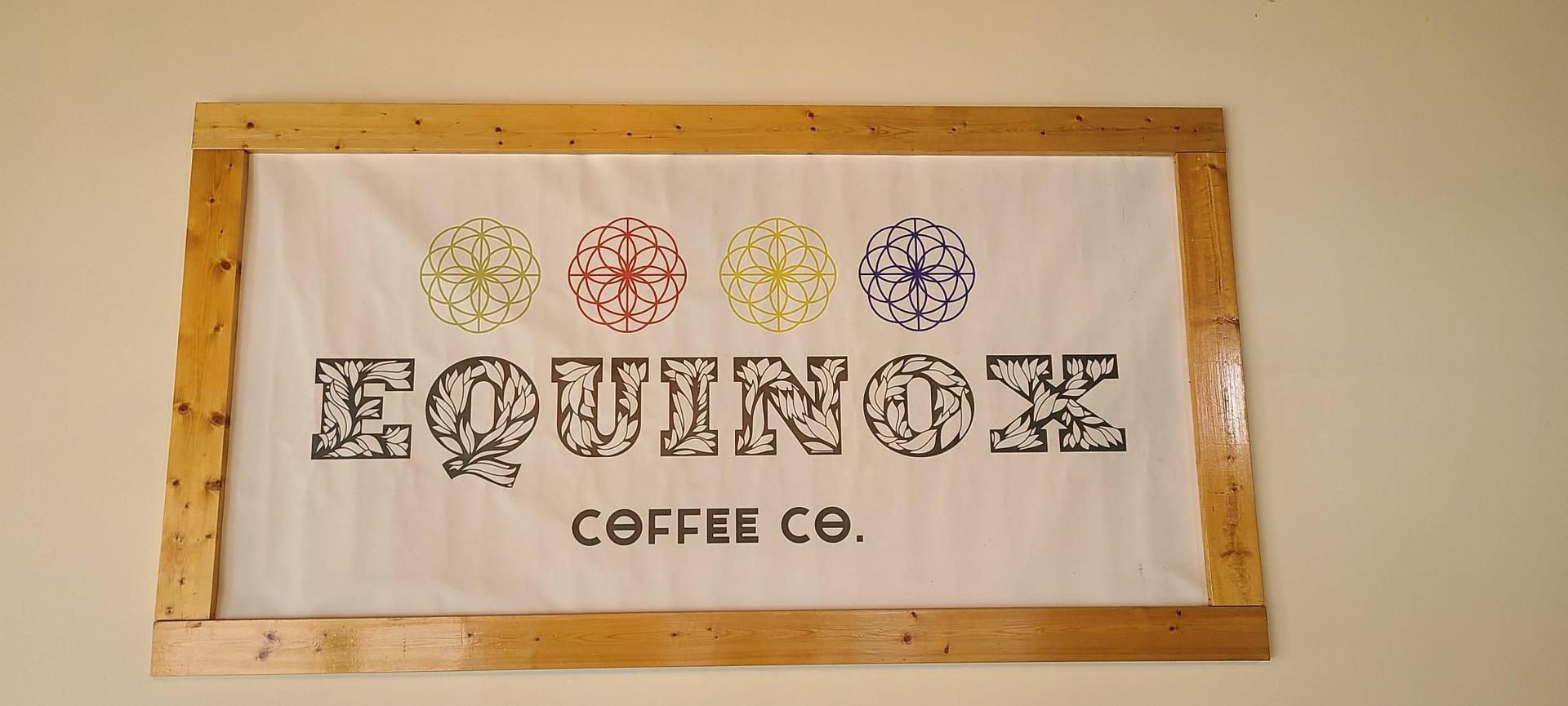 A framed sign for 'EQUINOX COFFEE CO.' with colorful geometric patterns.