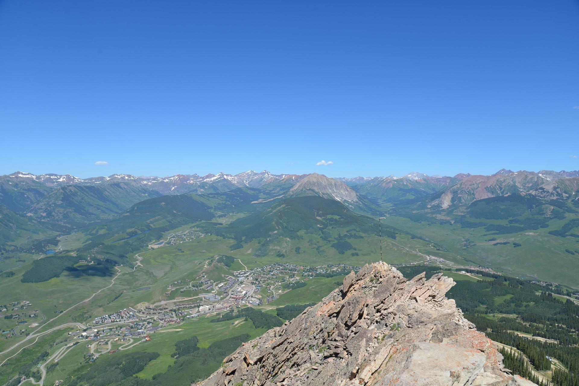 Expansive mountain panorama from a rocky summit overlooking a valley town.