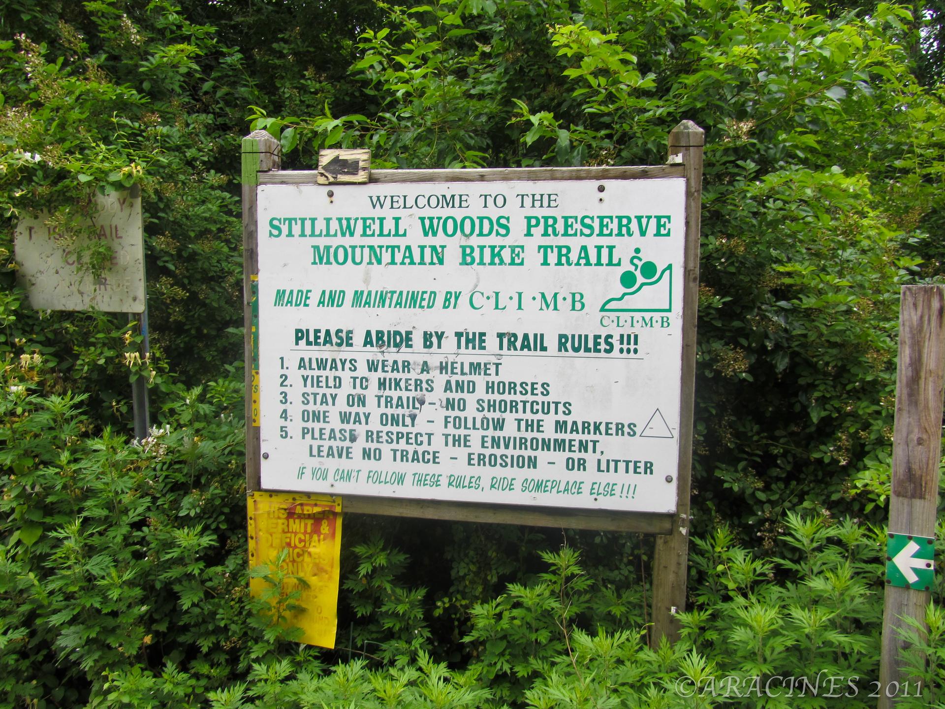 A white sign with green text stands amidst dense green foliage.