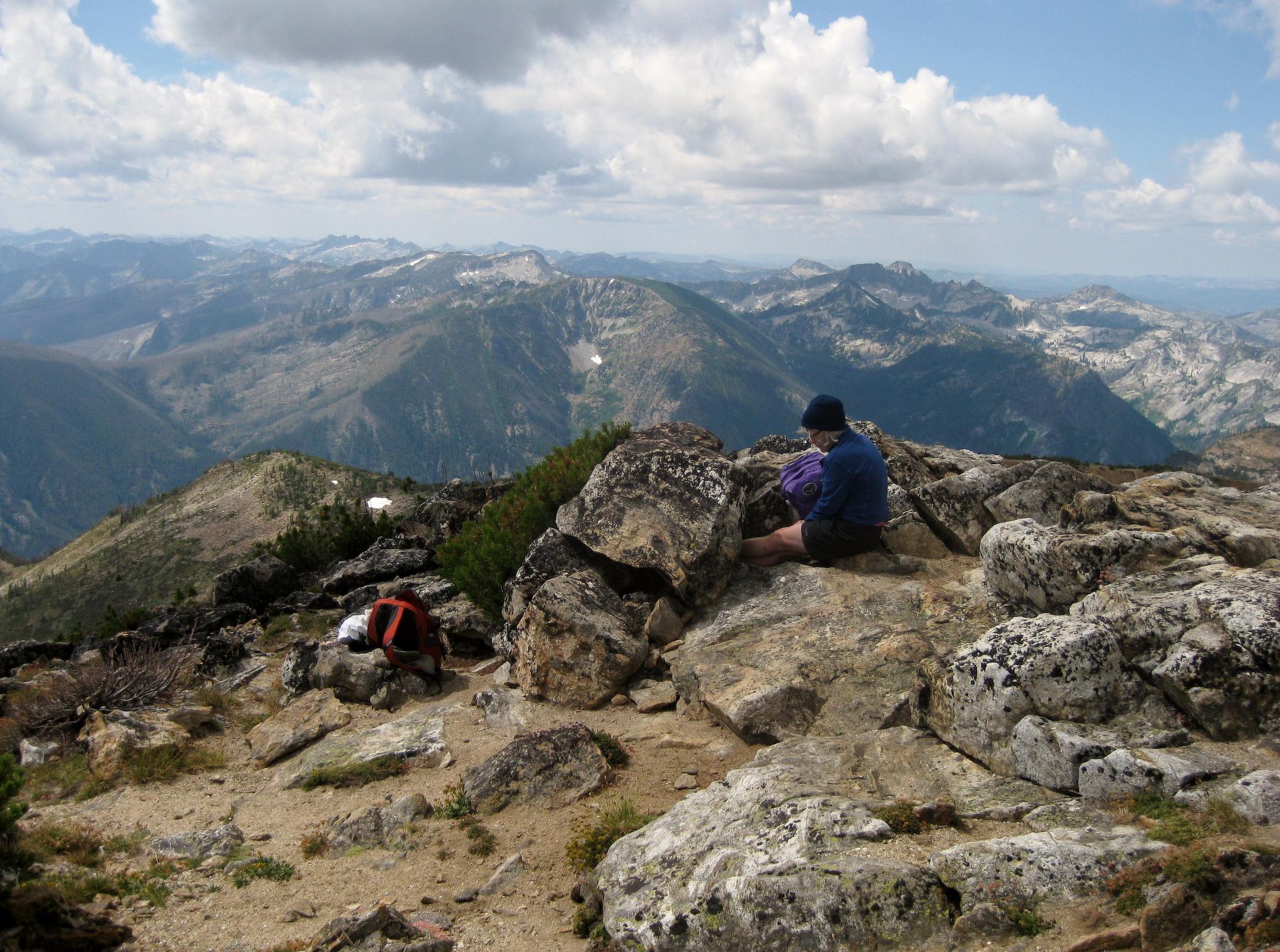 Two people resting on a rocky mountain peak overlooking a vast range.
