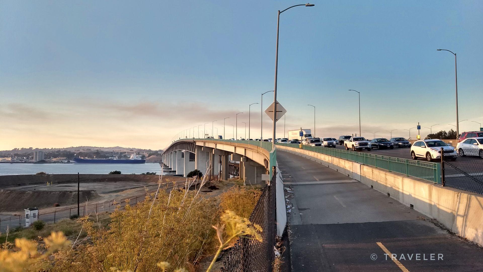 Cars on a bridge over water during golden hour, with a hazy sky.