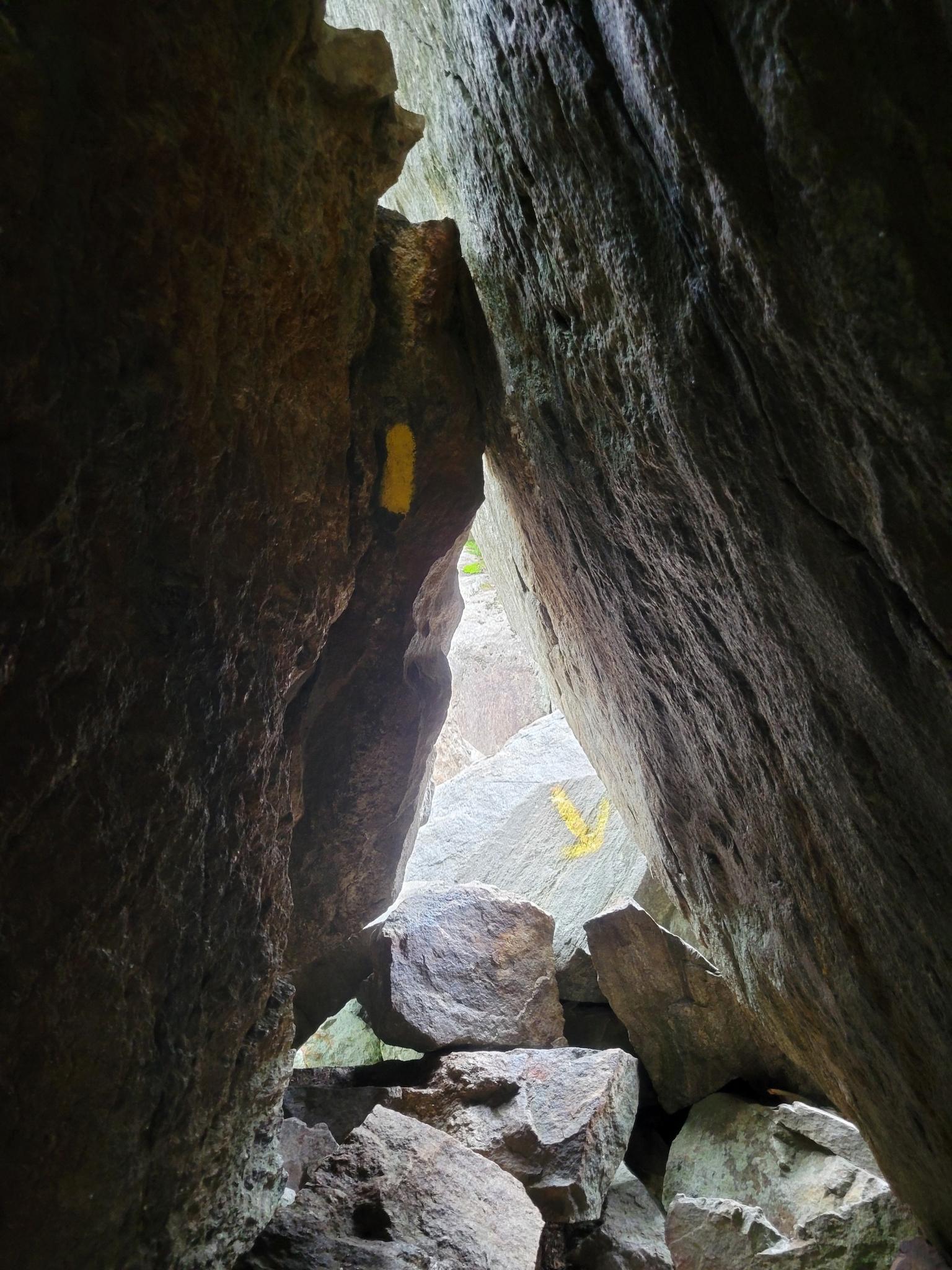 Narrow rock crevice with yellow trail blazes leading to a bright opening.