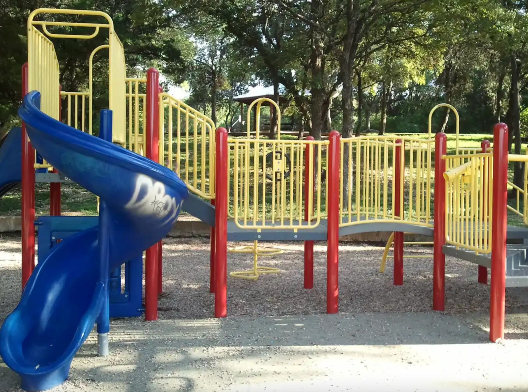 A colorful playground with blue slides and yellow railings under dappled sunlight.