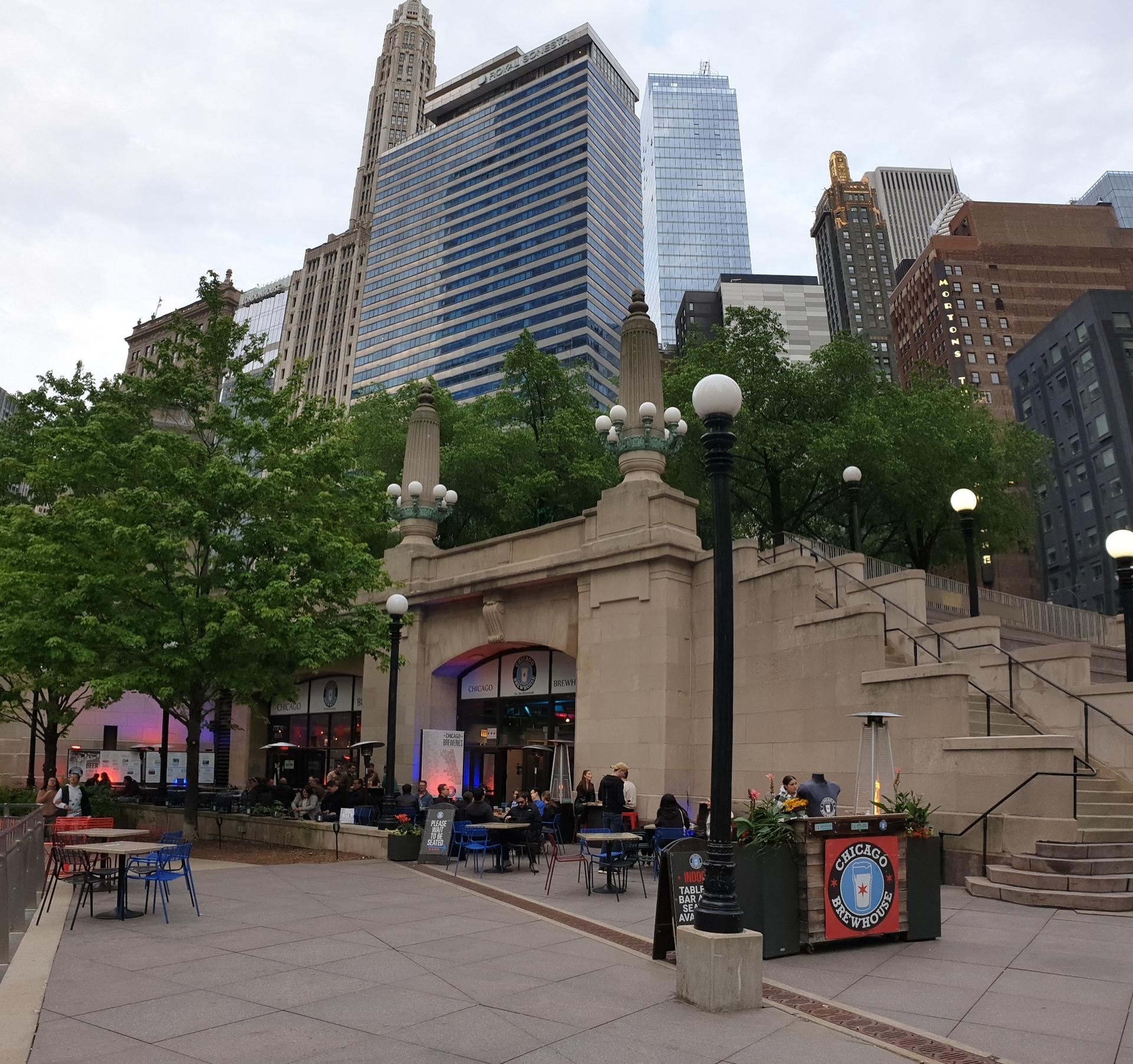 People dine at an outdoor patio with stone architecture and tall city buildings.