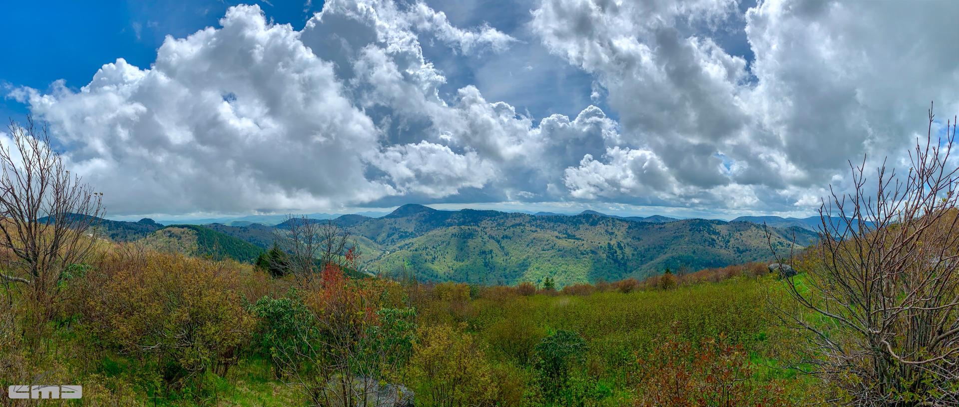 Panoramic view of green mountains under a bright, cloudy sky.