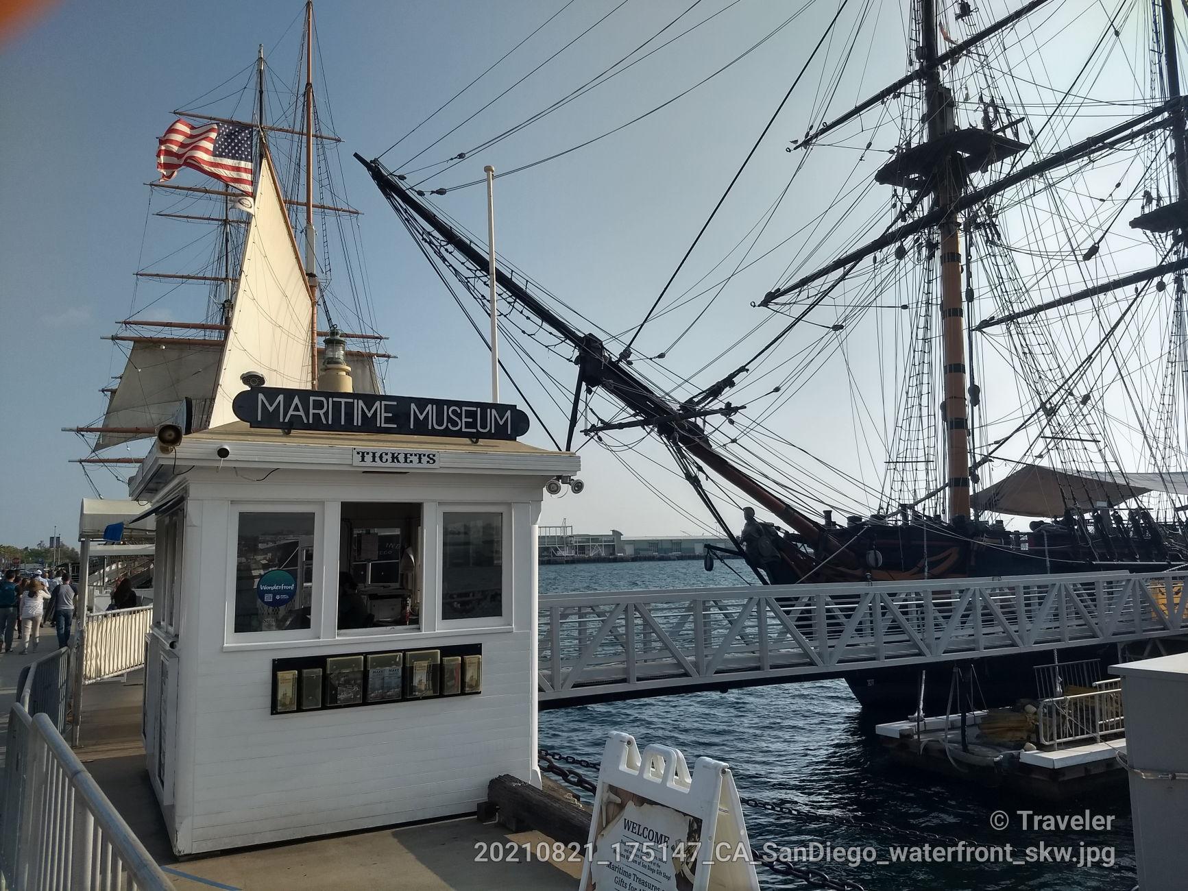 A white ticket booth next to a large, historic tall ship at a dock.