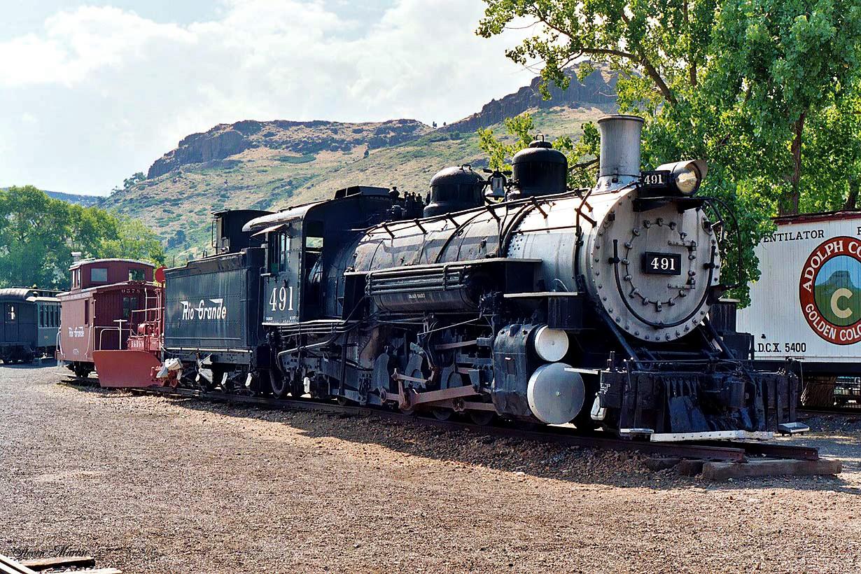 Large black steam locomotive parked on tracks, with a rocky hill behind.