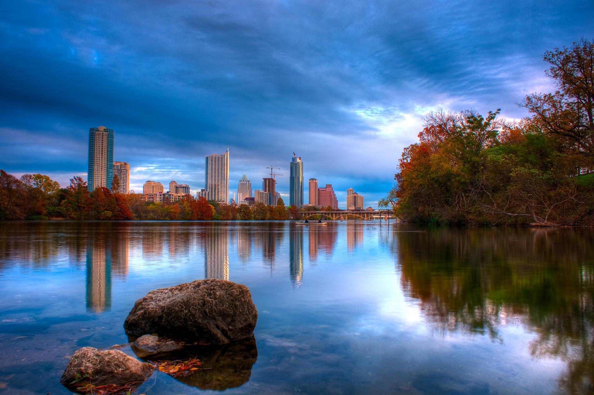 City skyline reflected in a calm river with colorful autumn trees. Dramatic sky.