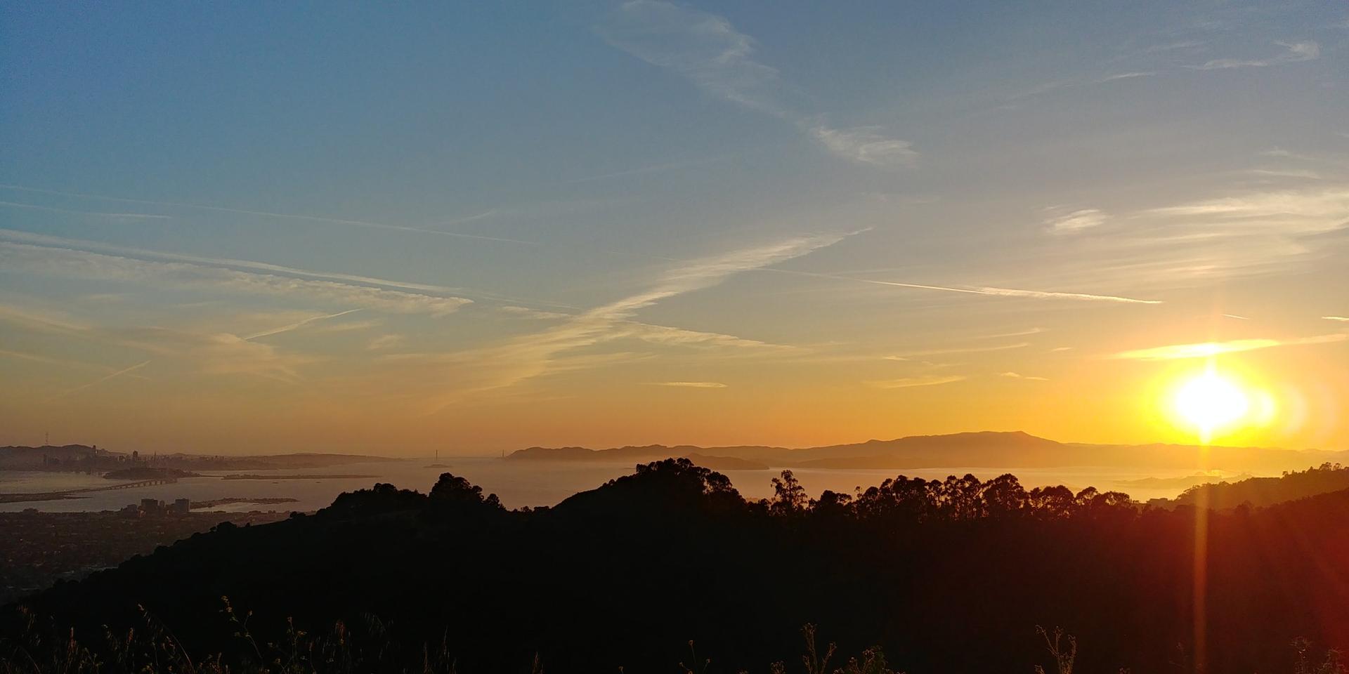 Golden sunset over distant water and silhouetted hills, with a clear sky.