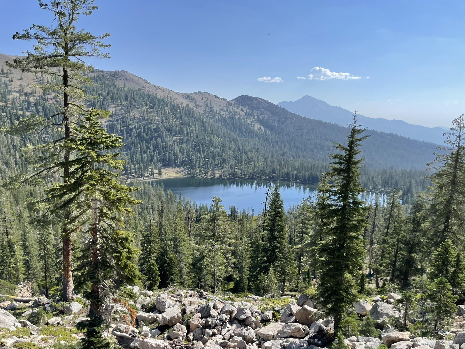 A serene lake surrounded by pine forests and mountains under a bright sky.