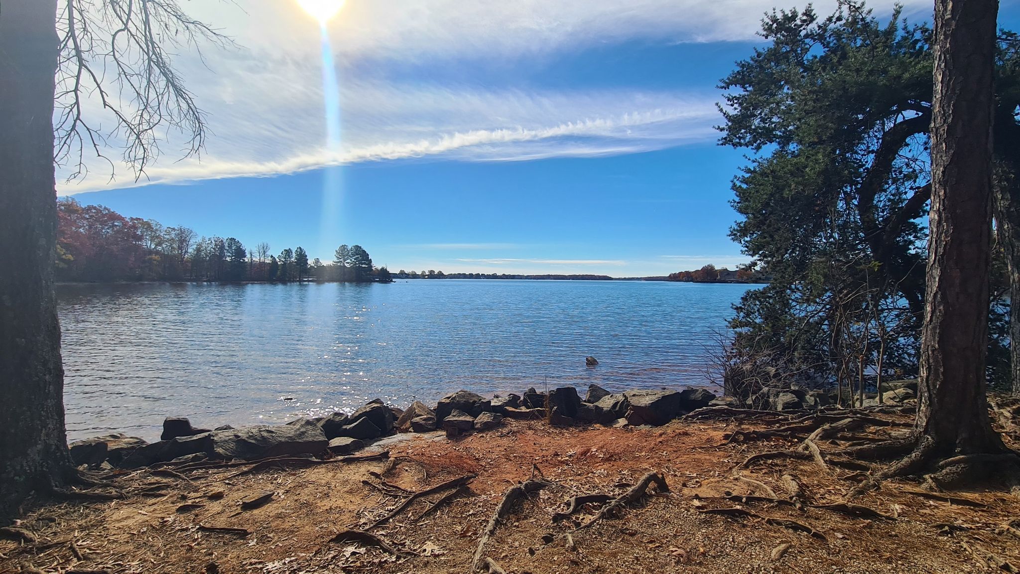 Sunny lake view from a rocky shore, framed by trees. - Ramsey Creek Loop