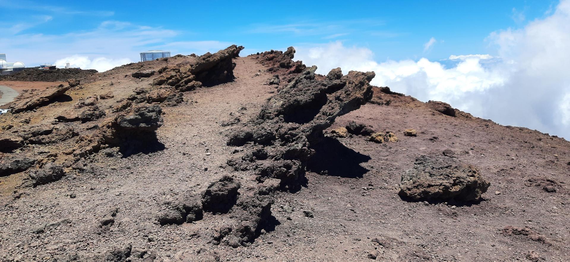 Jagged dark rocks on a reddish-brown, barren hillside with clouds in the distance.