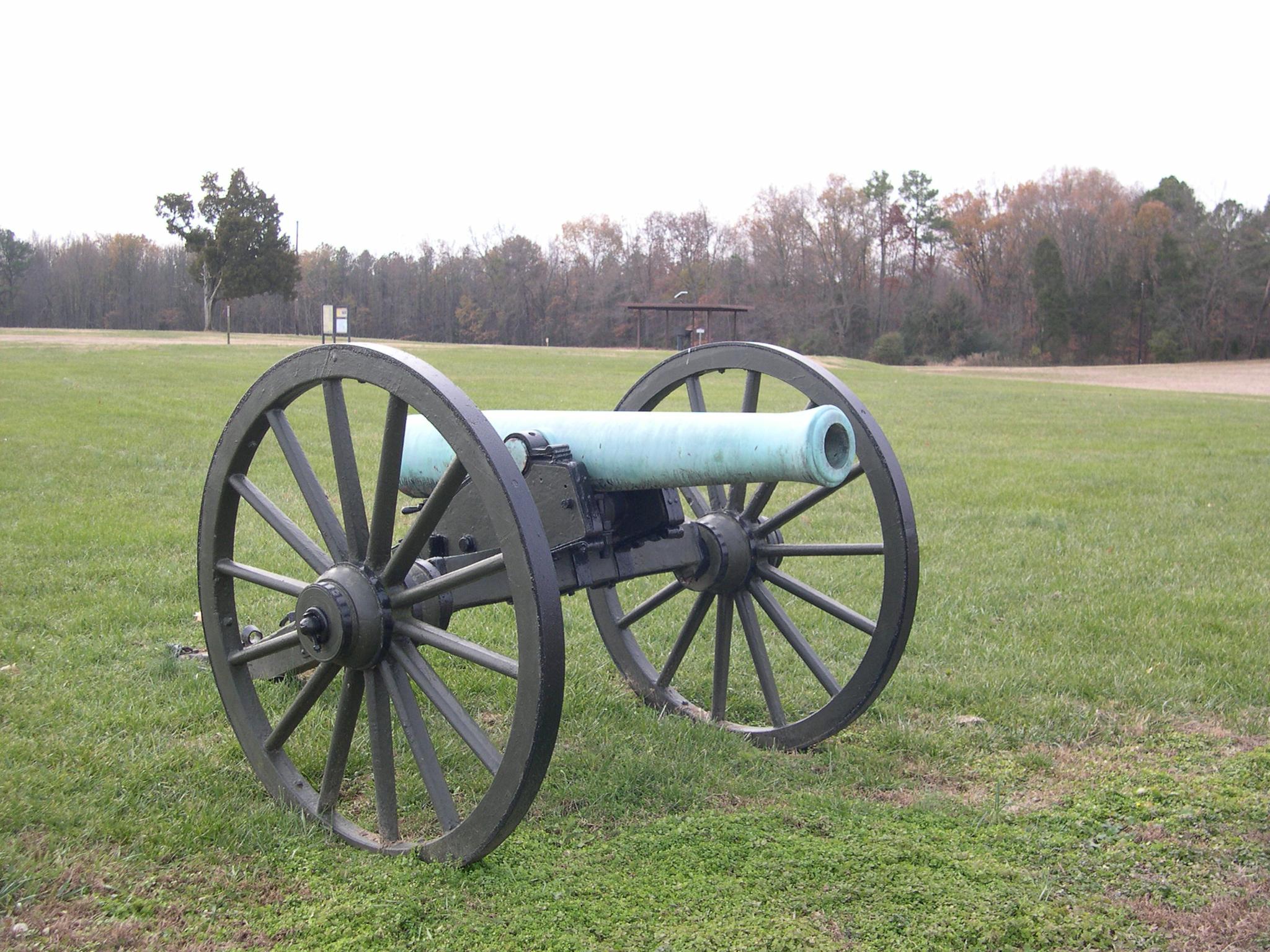 Historic cannon with large wooden wheels on a green grassy field.