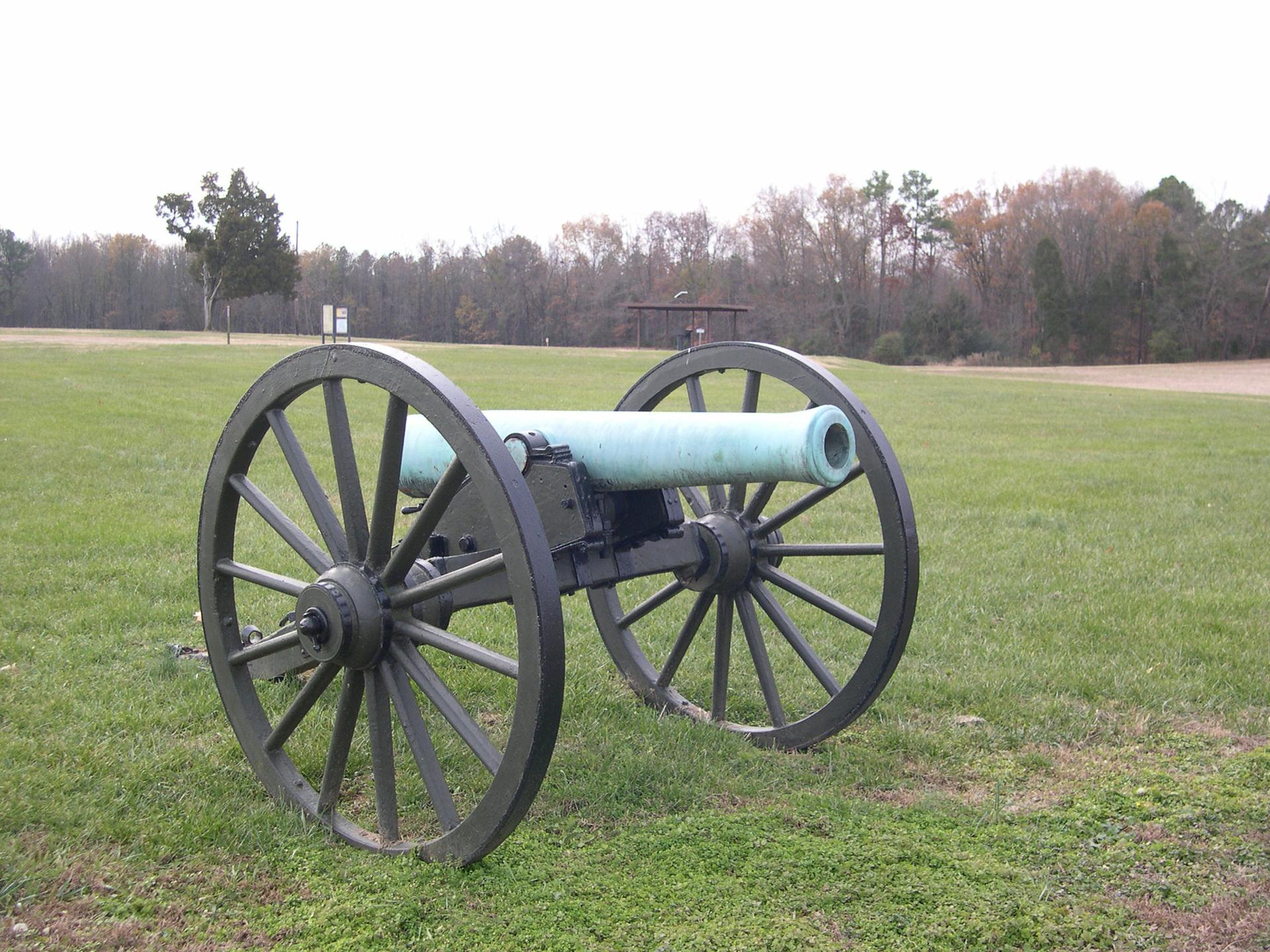 Historic cannon with large wooden wheels on a green grassy field.