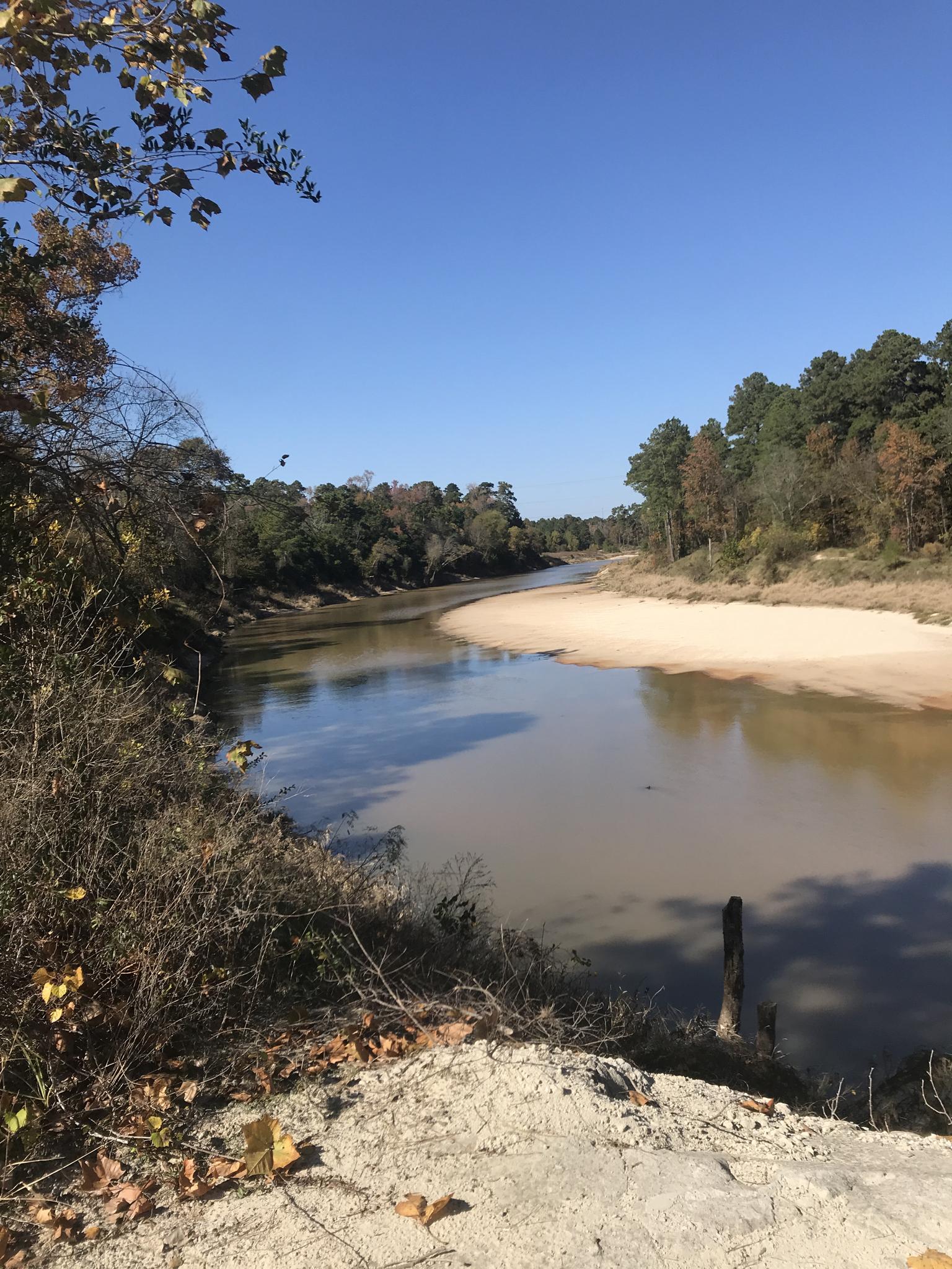 Wide river with sandy banks and autumn trees under a bright blue sky.