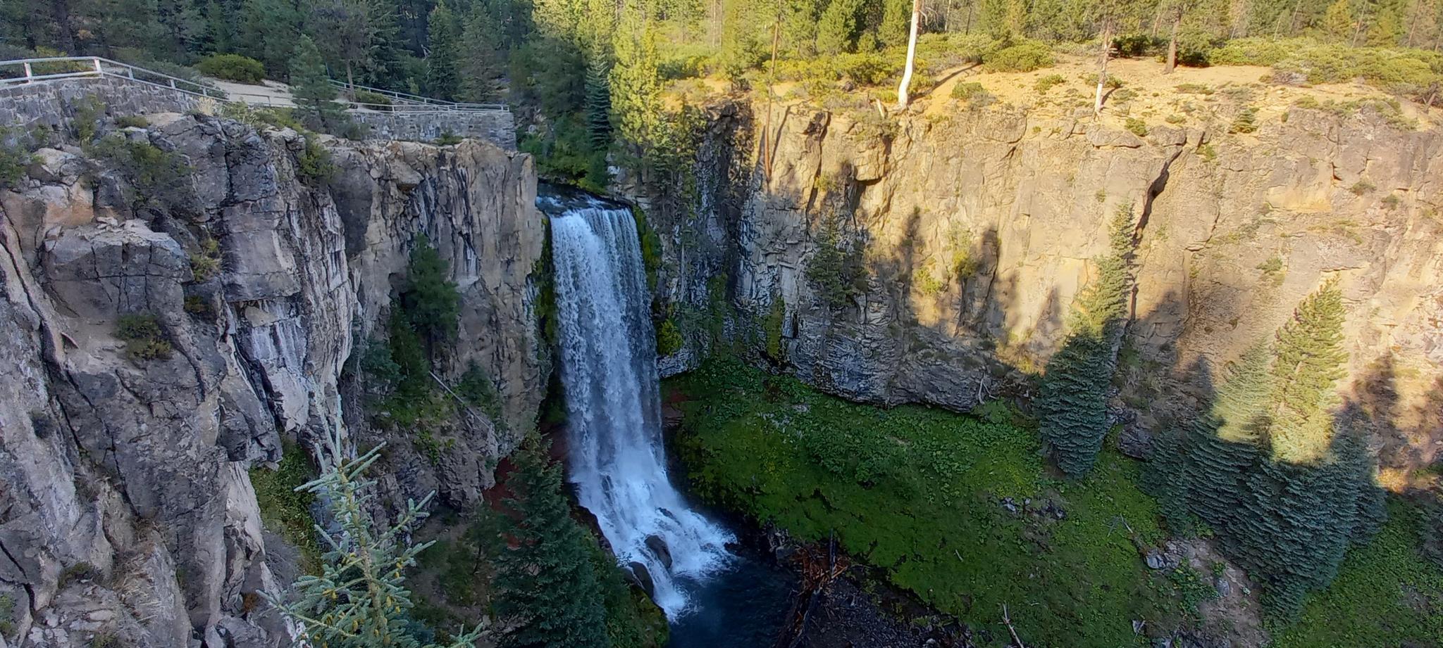 Waterfall plunging over rocky cliffs into a river, bathed in sunlight.