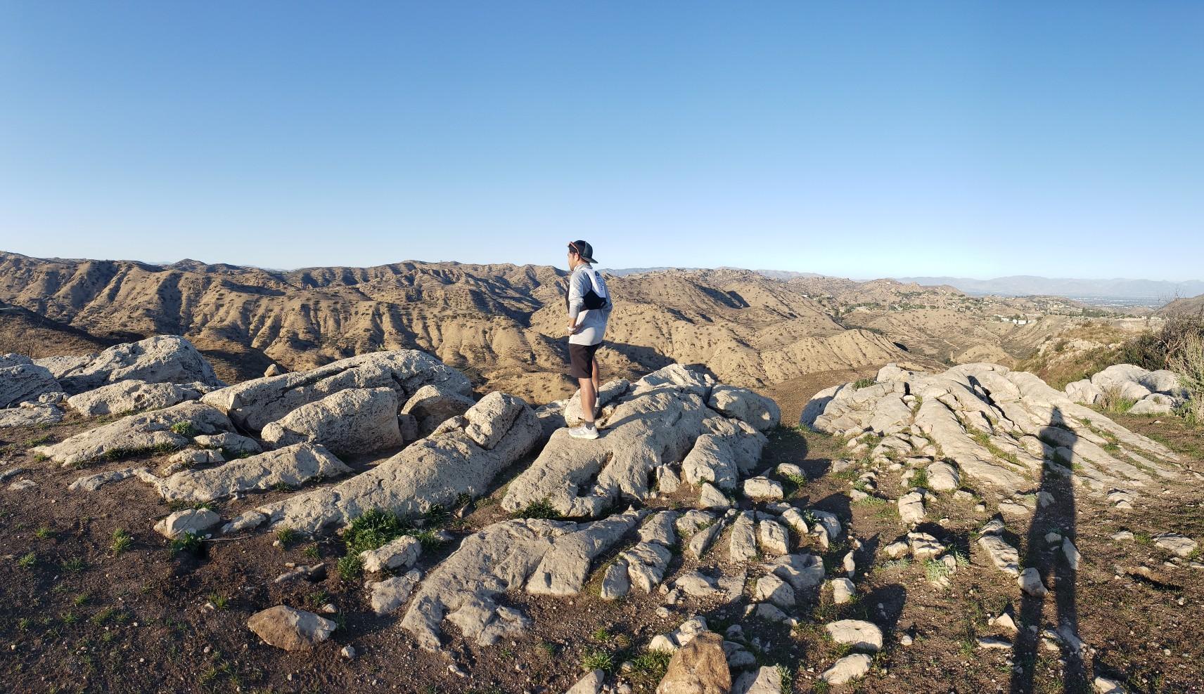 Person stands on rocky terrain, observing the vast arid landscape under a clear sky.