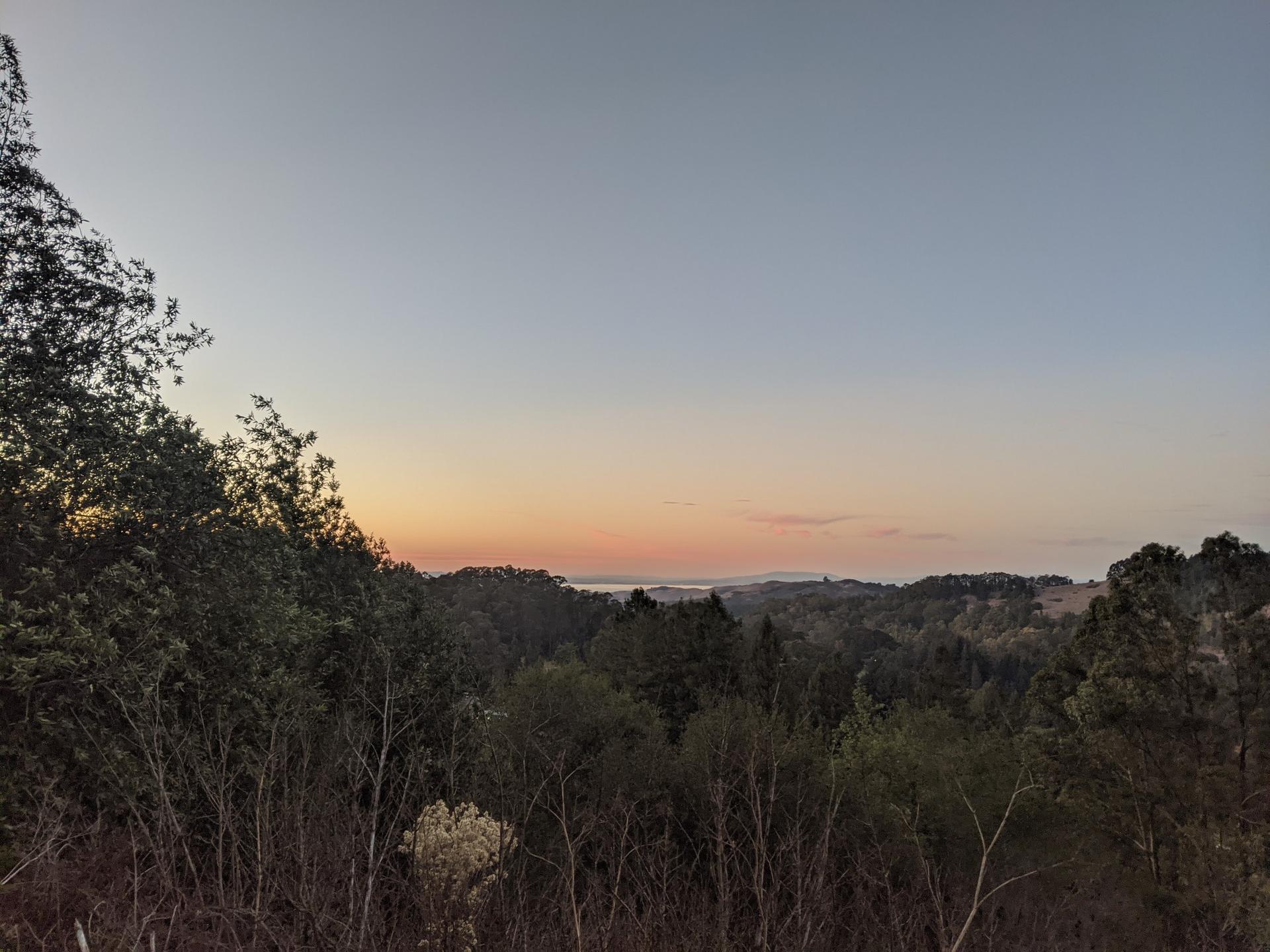 Forested hills at sunset with a warm glow on the distant horizon.