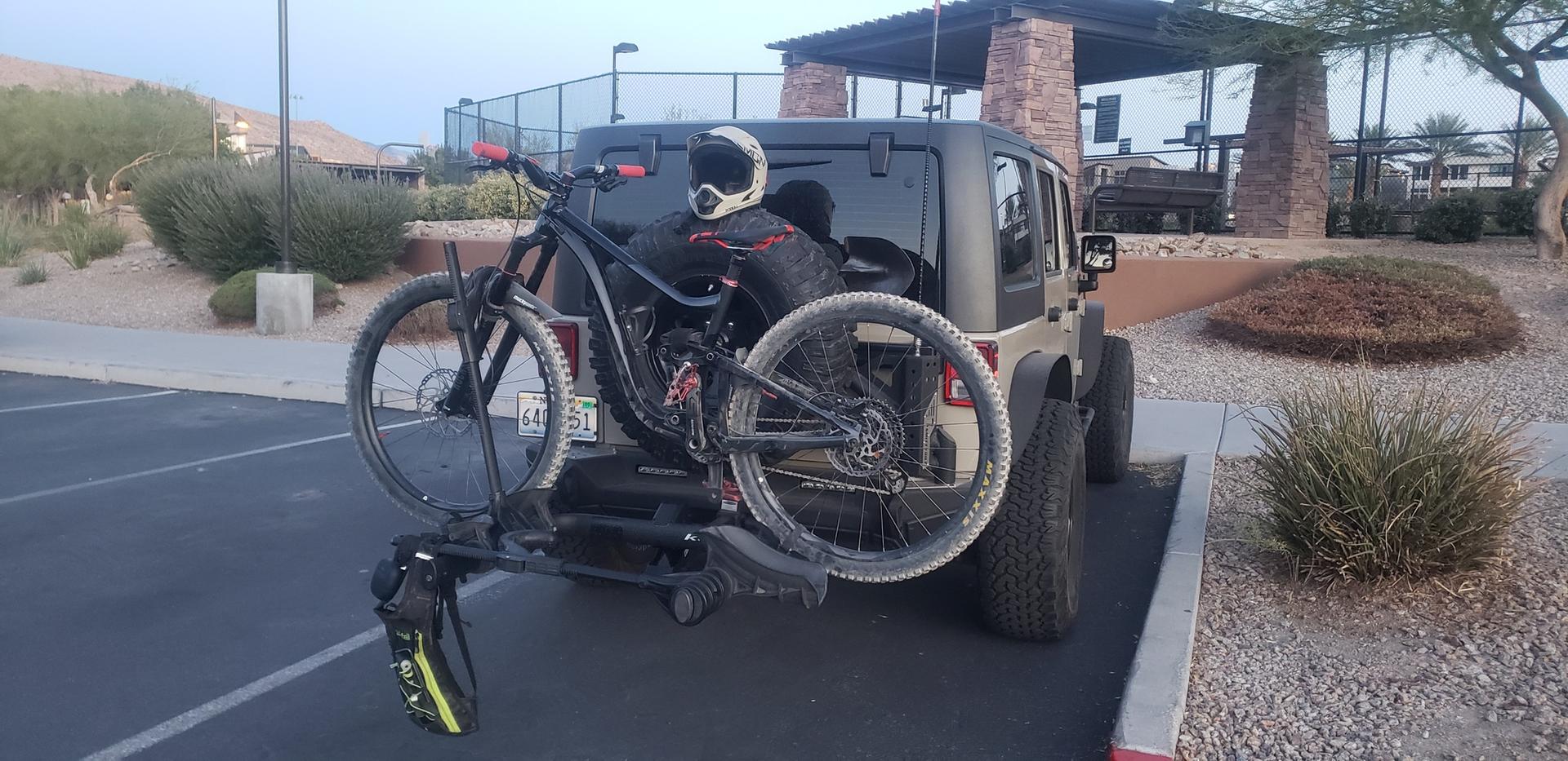 Jeep with a mountain bike on a rack, person in helmet nearby.