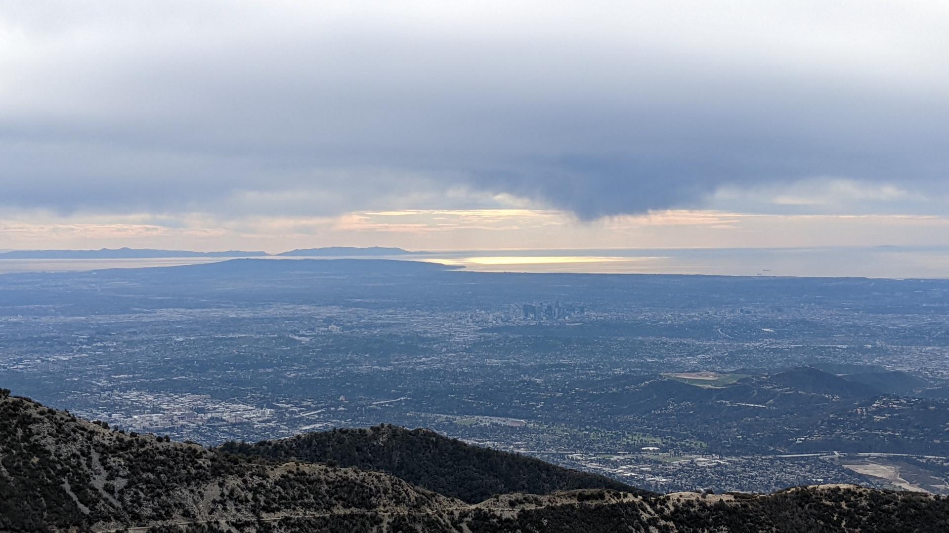 Panoramic view of a city stretching to a sunlit ocean under a cloudy sky.