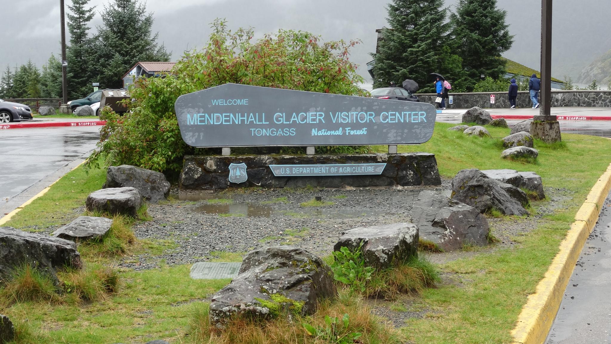 Large welcome sign surrounded by rocks and grass on a wet, overcast day.