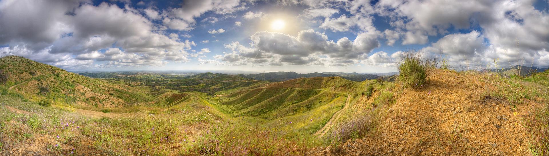 Panoramic view of rolling green and brown hills under a bright, cloudy sky.