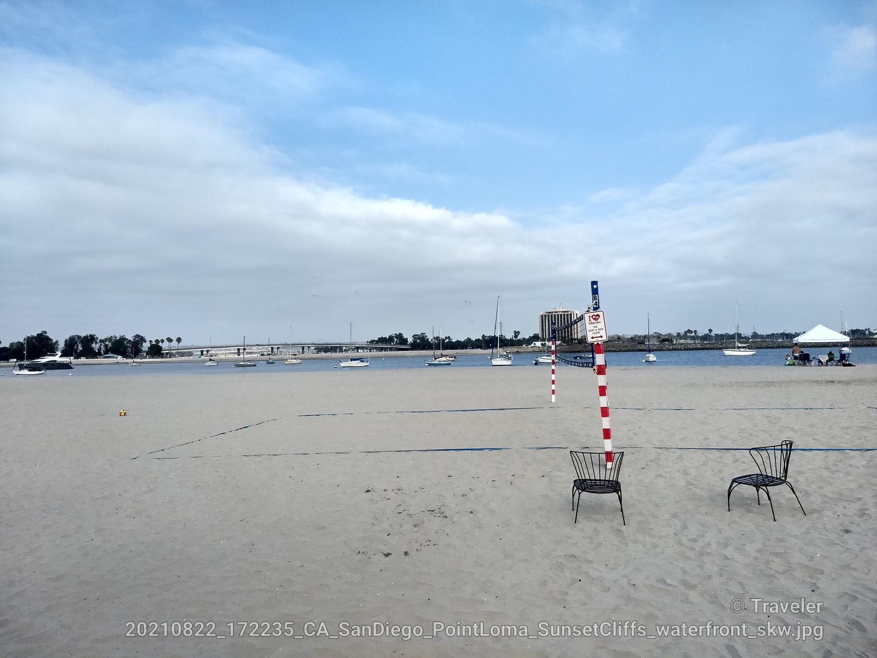 Bright beach scene with a volleyball net, chairs, and calm water.
