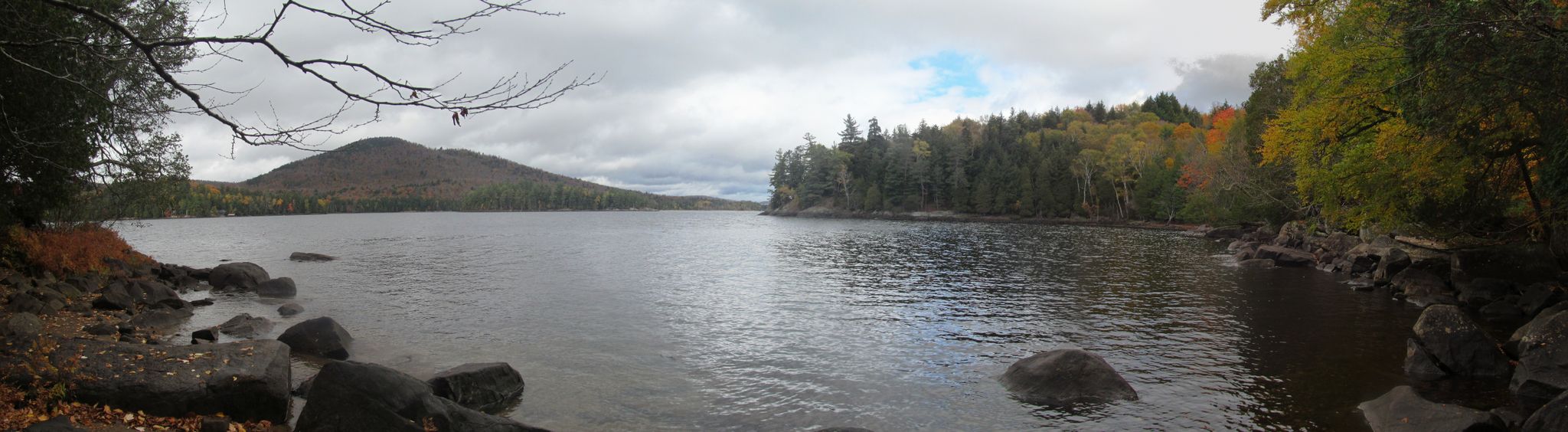 Lake with rocky shore, autumn trees, and distant mountain under an overcast sky. - Long Lake via Northville-Placid Trail