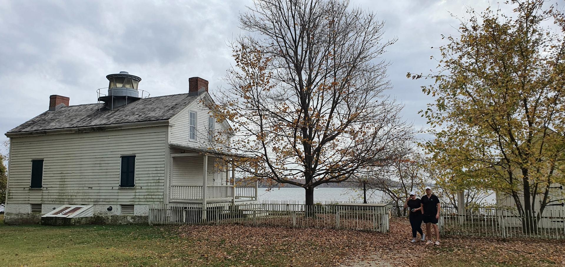 Old white house with bare trees, two people, cloudy day.