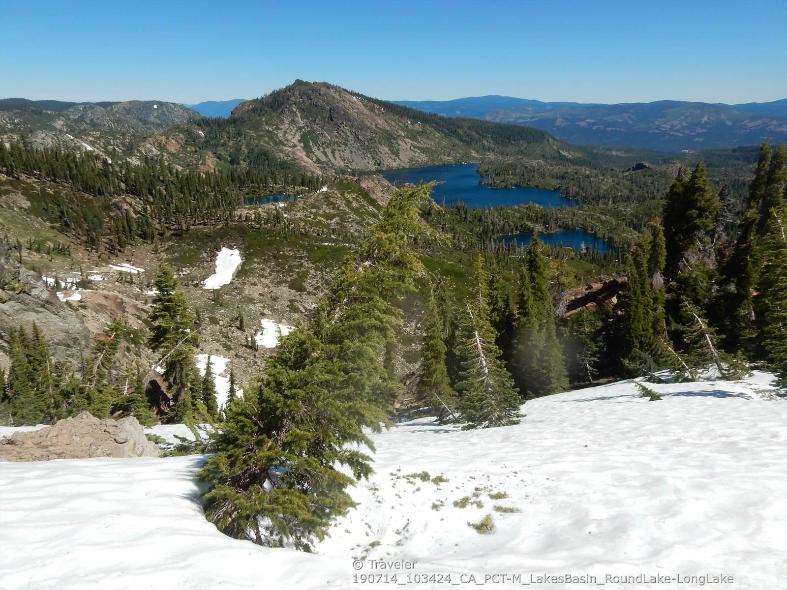 Snowy foreground overlooking multiple blue lakes, green forests, and mountains.