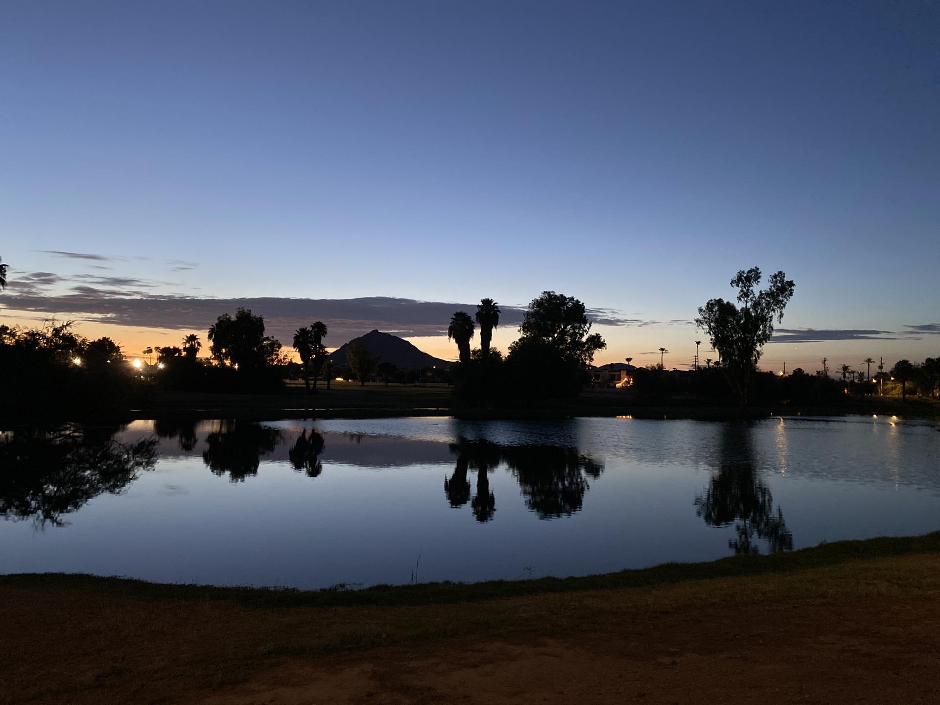 A serene lake reflecting a colorful sunset sky with silhouetted trees.