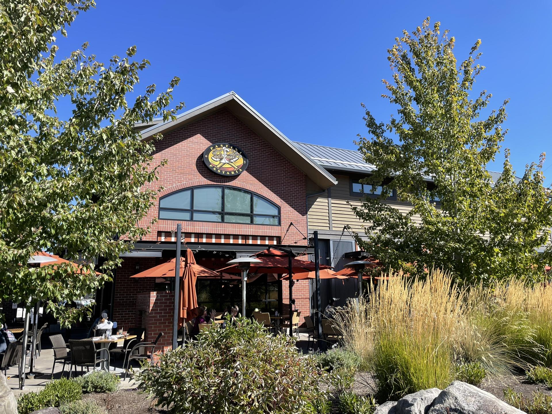 Brick building with outdoor patio seating, surrounded by green trees.