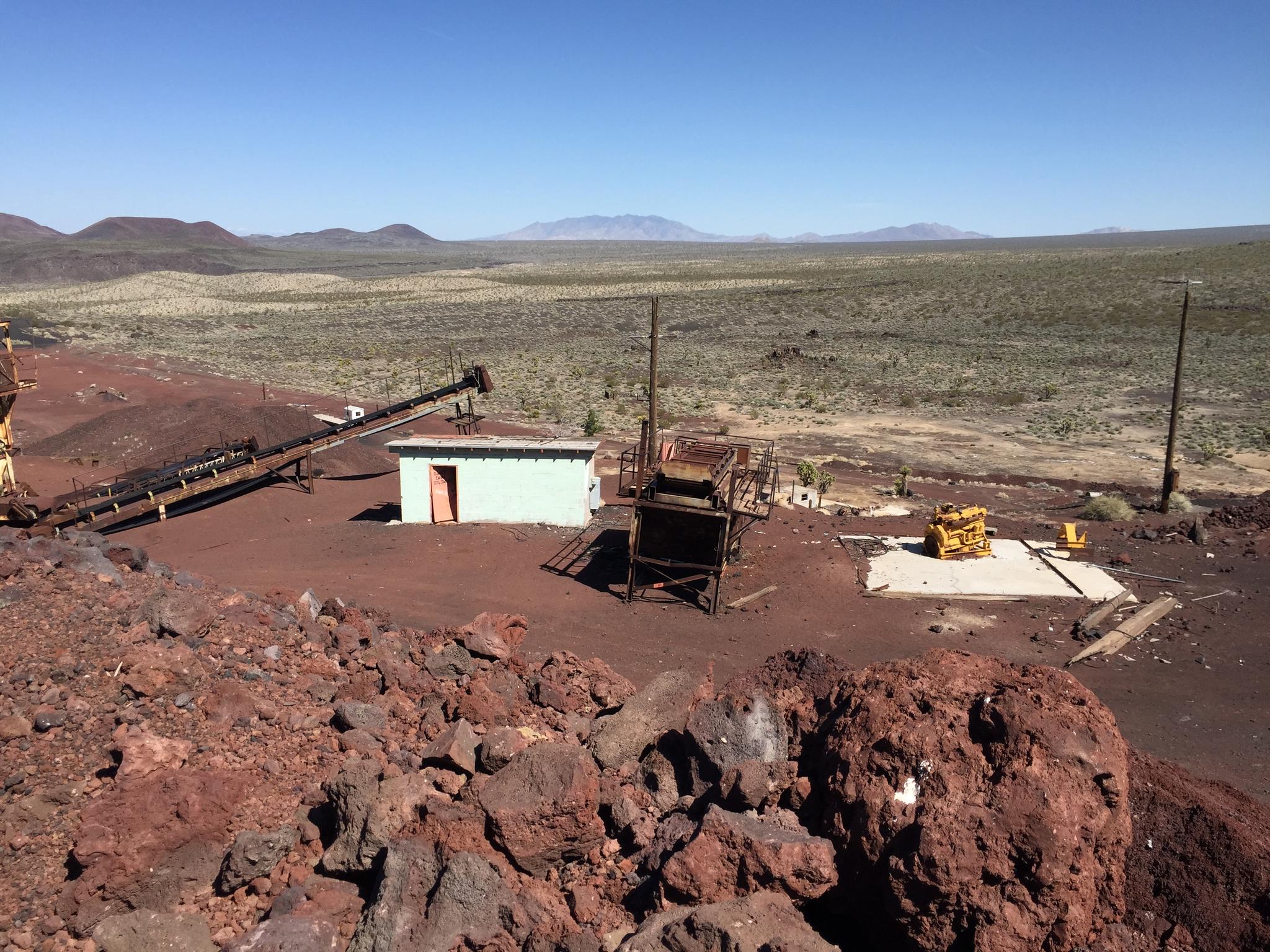 Abandoned industrial buildings and machinery sit in a vast, rocky desert landscape.