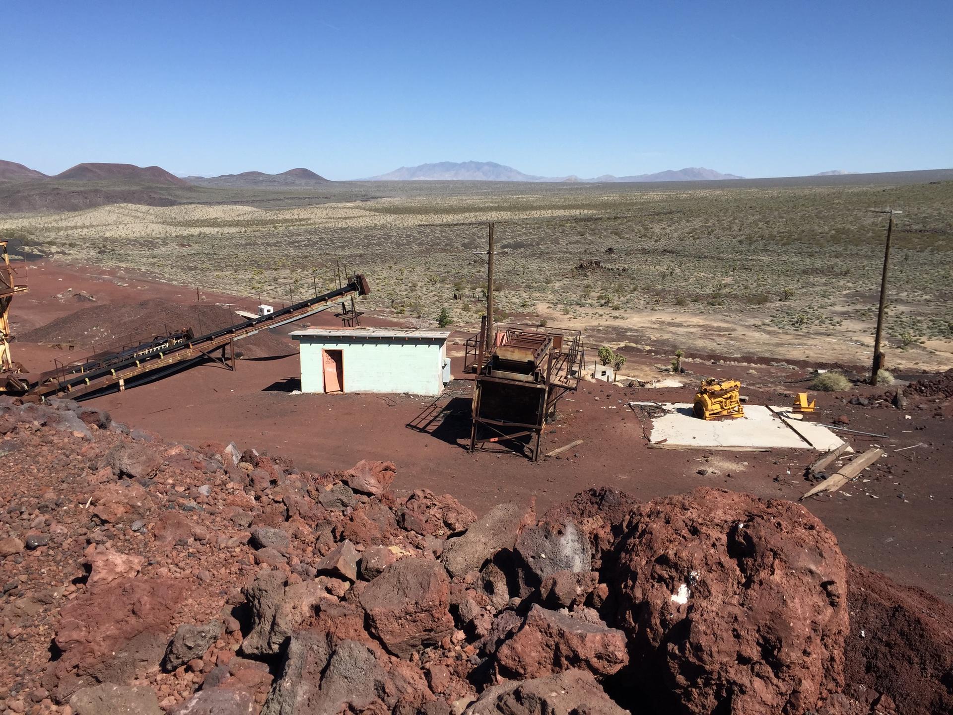 Abandoned industrial buildings and machinery sit in a vast, rocky desert landscape.