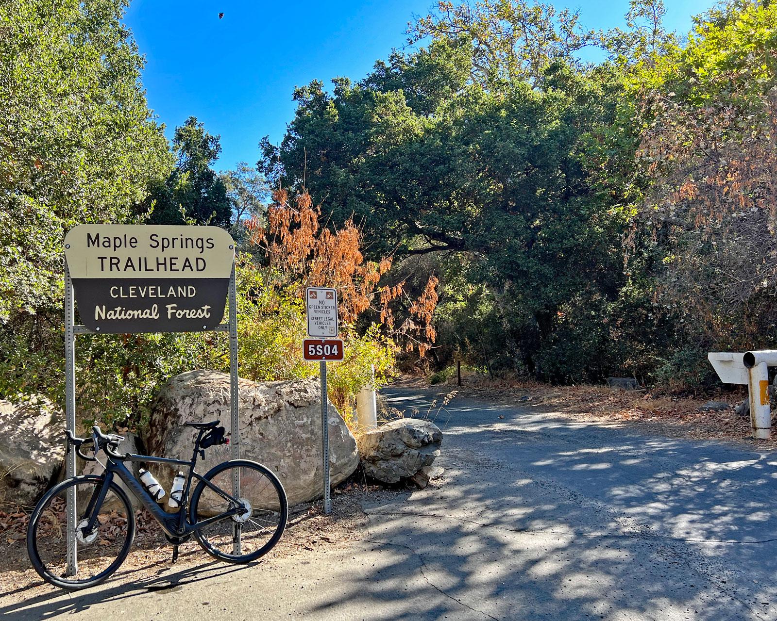 A bicycle is parked next to a sign at the edge of a wooded area.