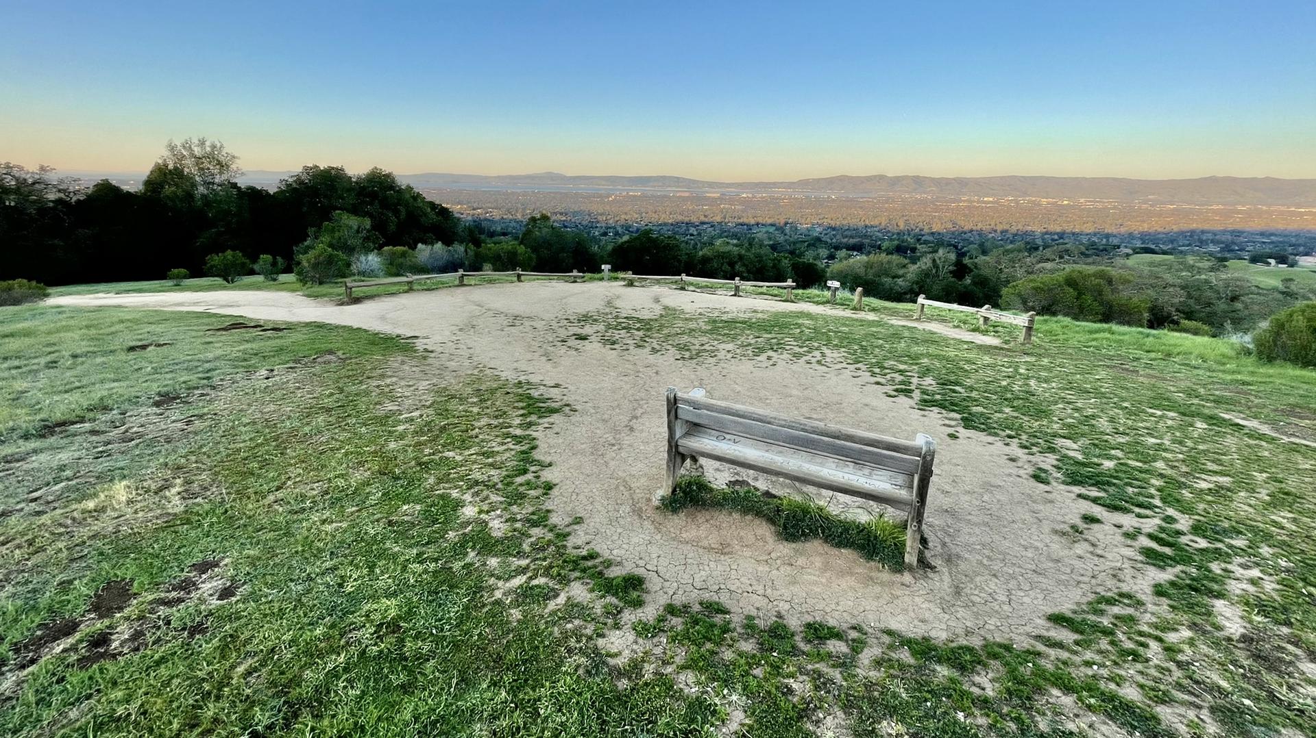 Wooden bench on a grassy hilltop overlooking a distant valley at dawn.