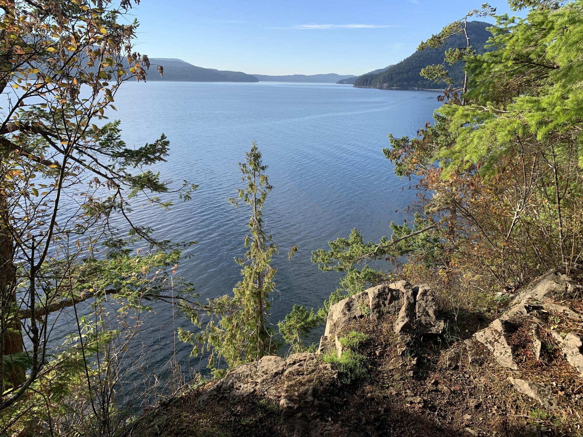 Sunny view of a wide blue lake framed by green trees and rocky cliffs.