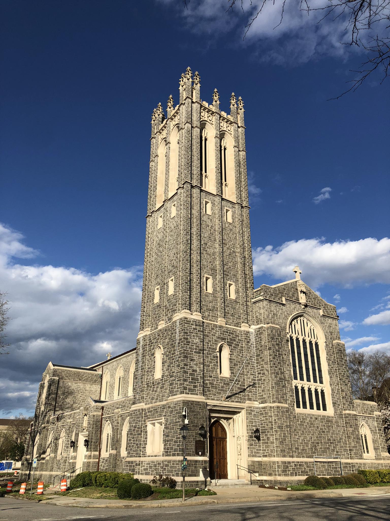 A large stone church with a tall tower under a partly cloudy blue sky.