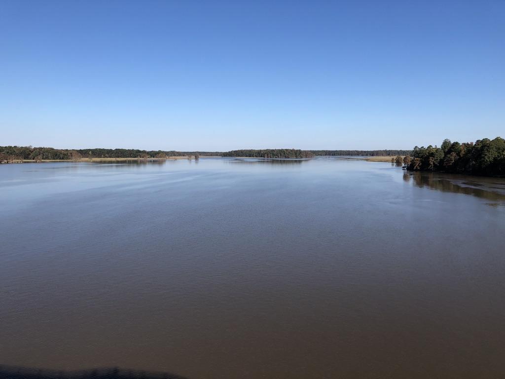A wide, calm river stretches to distant tree-lined banks under a clear blue sky.