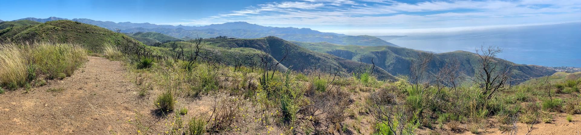 Panoramic view of rolling hills and distant ocean under a bright blue sky.