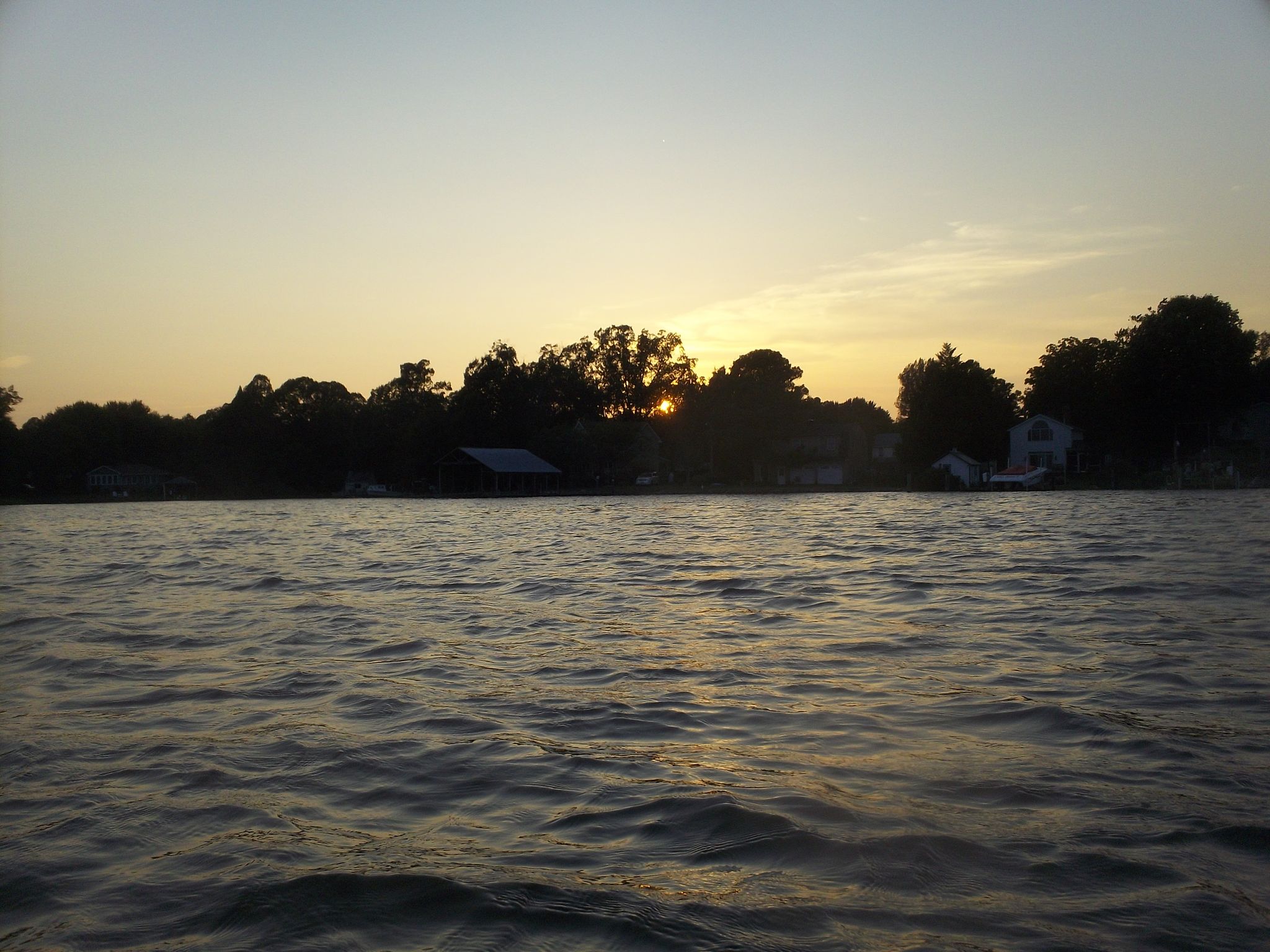 Sunset over a calm water body, silhouetting distant trees and houses. - Saint Michaels to Oxford loop