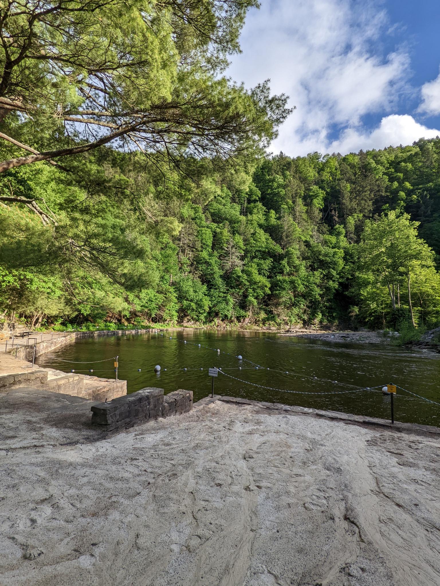 A sandy shore next to a calm lake surrounded by lush green forested hills.