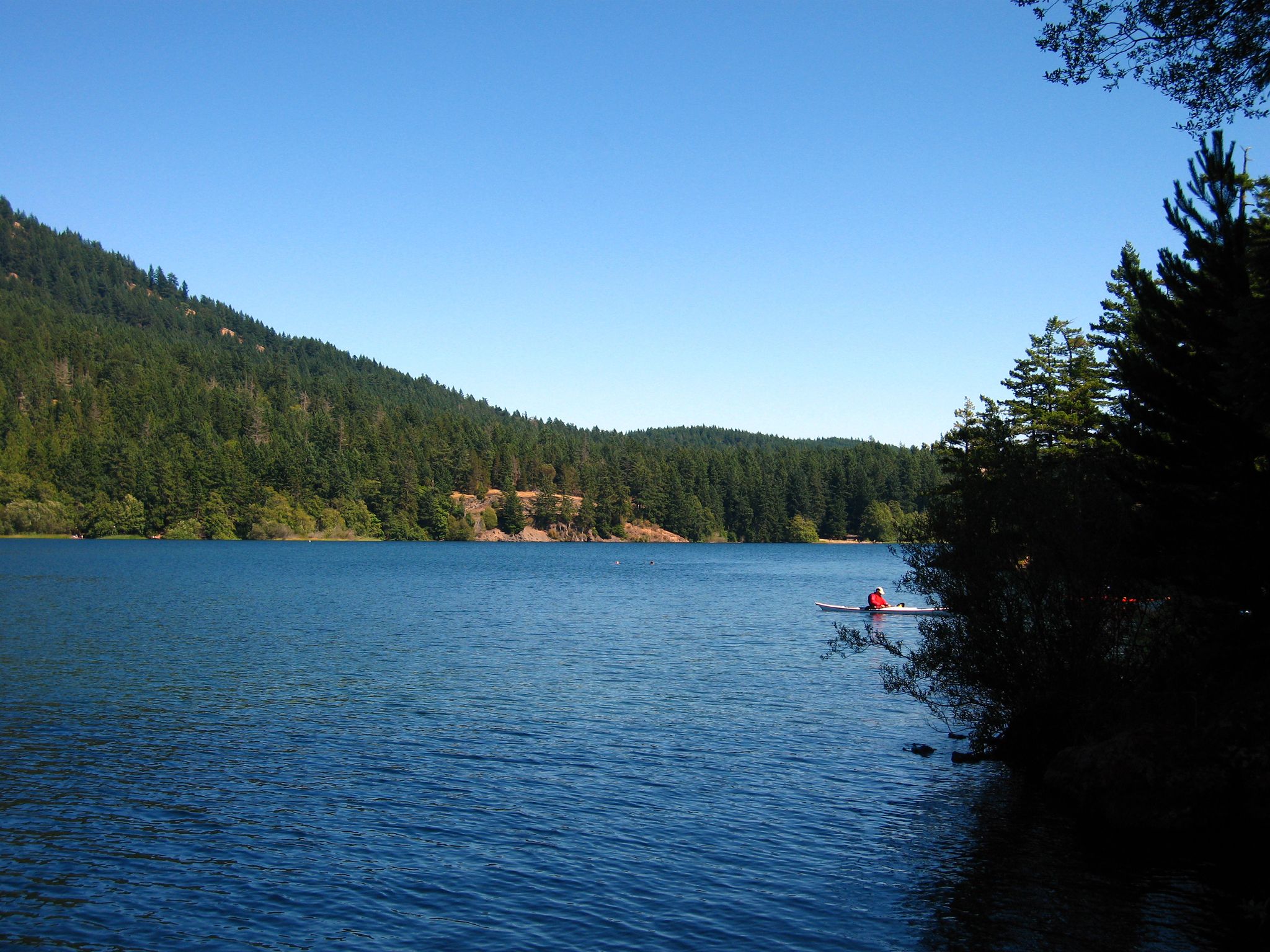 Sunny lake with forested hills, a kayaker near the shore. - Cascade Lake Loop Trail – Cascade Lake loop from Cascade Lake Dam