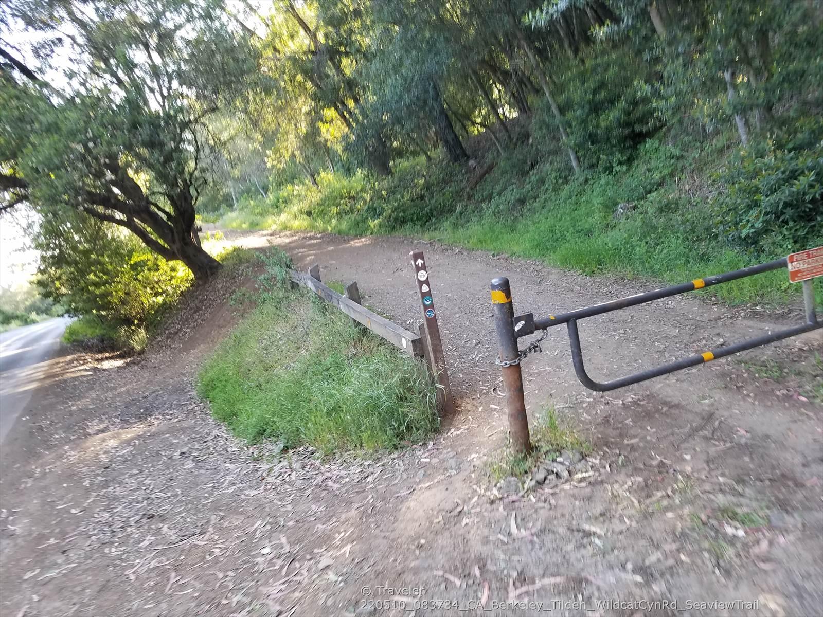 Dirt path leading to a closed metal gate and a wooden marker post.