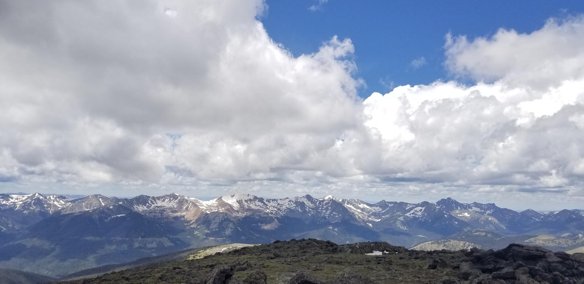 Panoramic view of snow-capped mountains under a dramatic blue and cloudy sky.