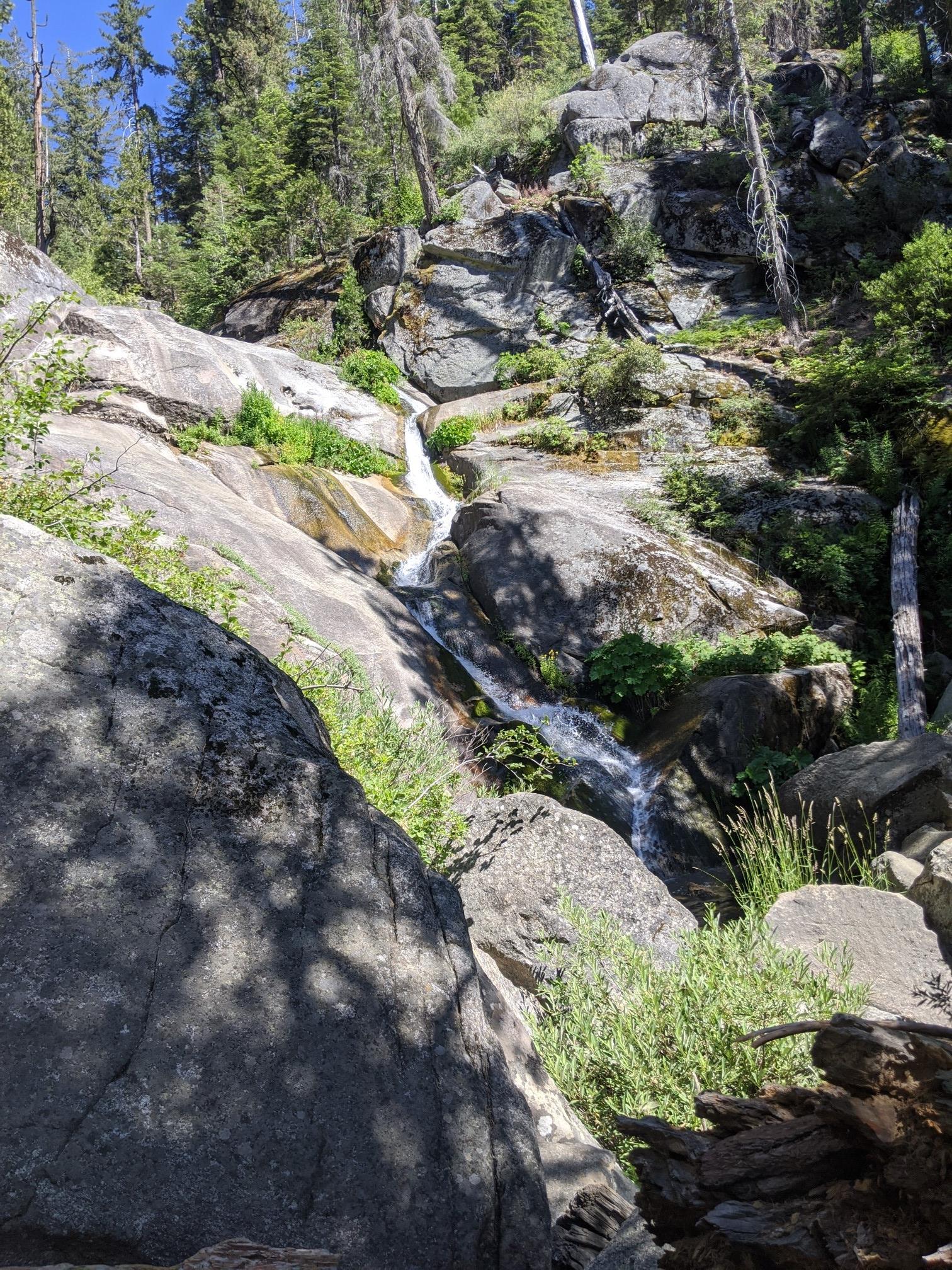 Waterfall cascading over large rocks in a sunlit forest.