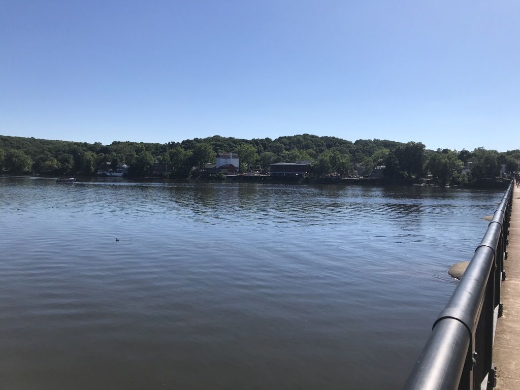 A wide river flows under a clear blue sky, with distant green hills. - New Hope-Lambertville Bridge – Stockton Inn loop from Ted Stiles Preserve at Baldpate Mountain