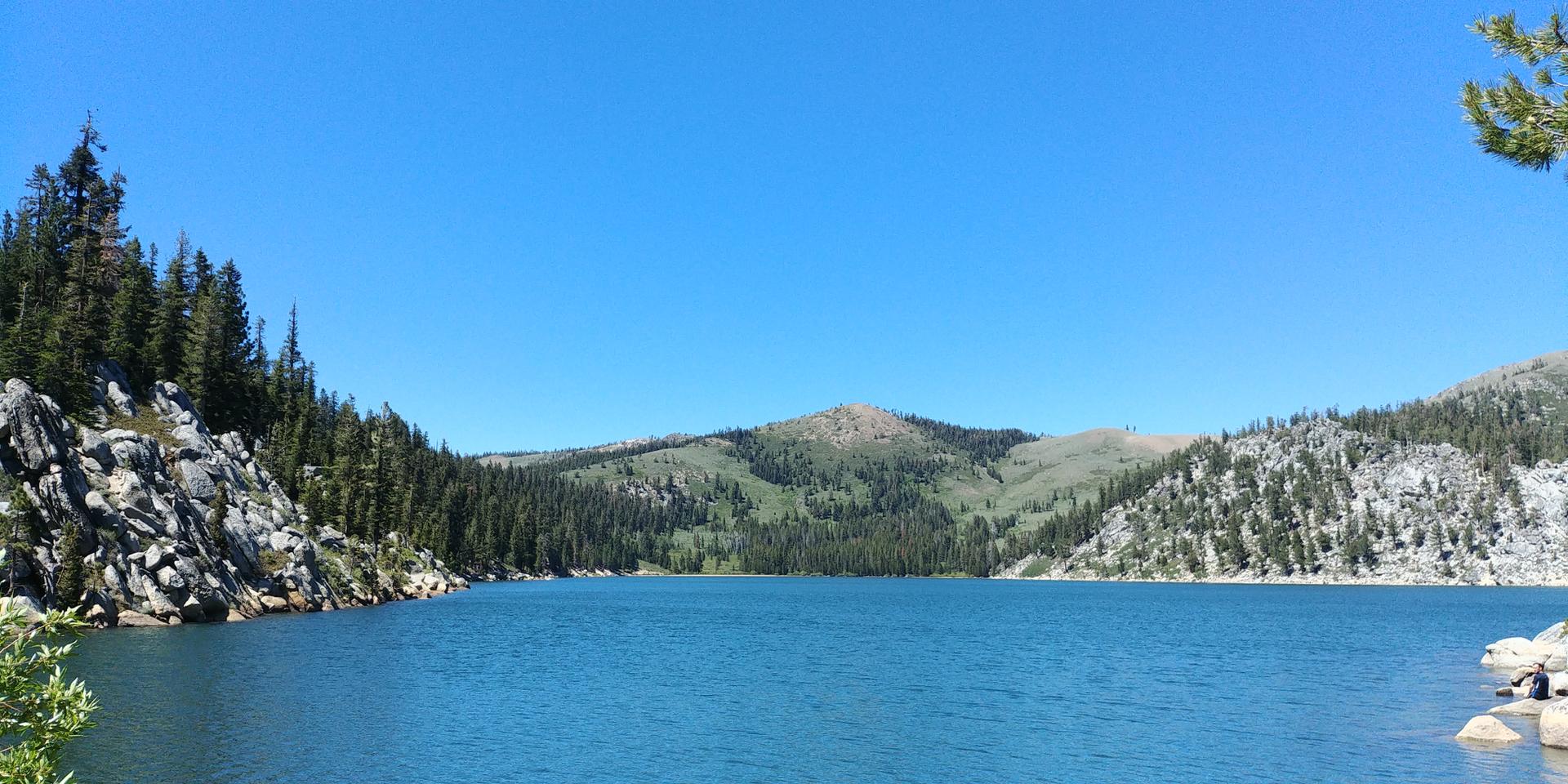 A vibrant blue lake nestled between rocky, forested mountains on a sunny day.